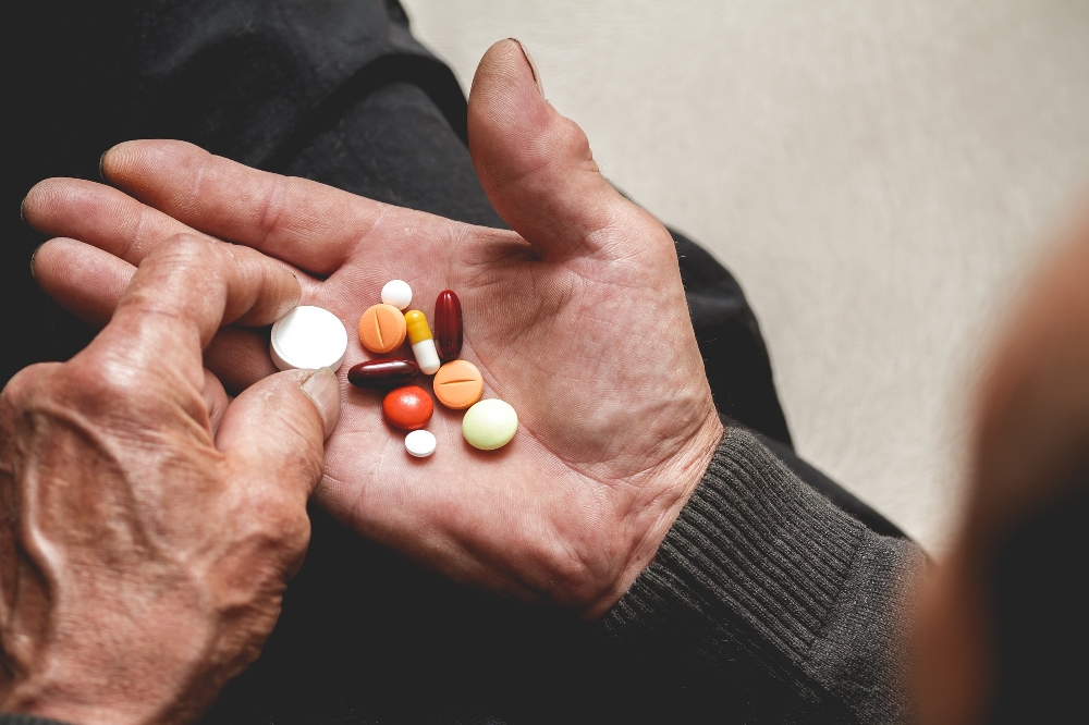 Elderly hand holds assorted pills, various colors.